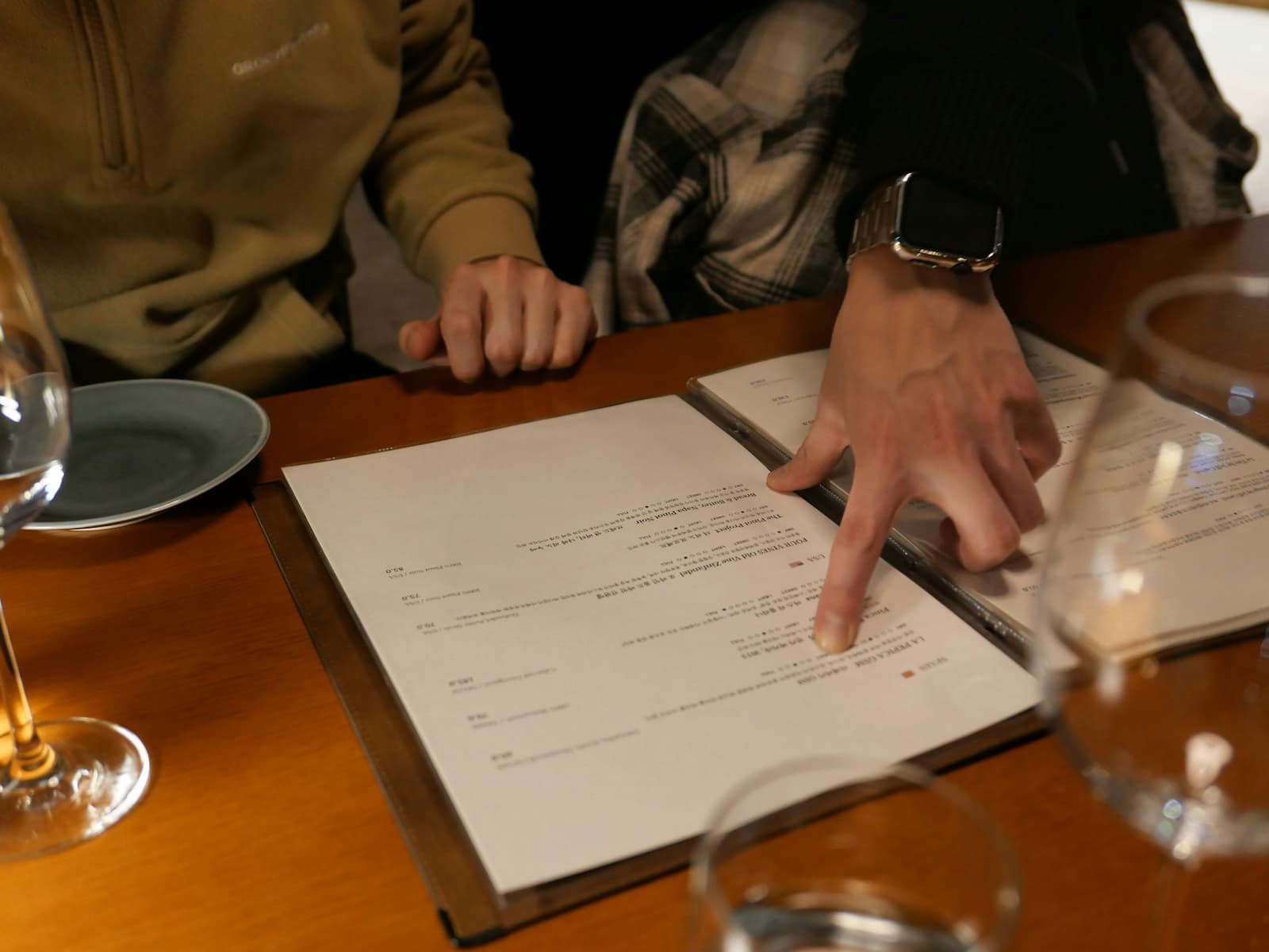 Close-up of two diners reviewing an open restaurant menu, with one person pointing to a menu item.